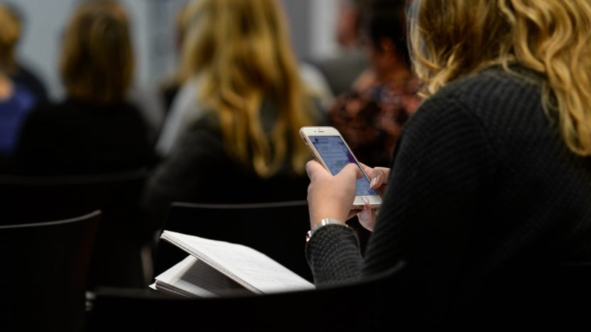 Eine Frau schaut auf einer Veranstaltung sitzend auf ihr Smartphone.